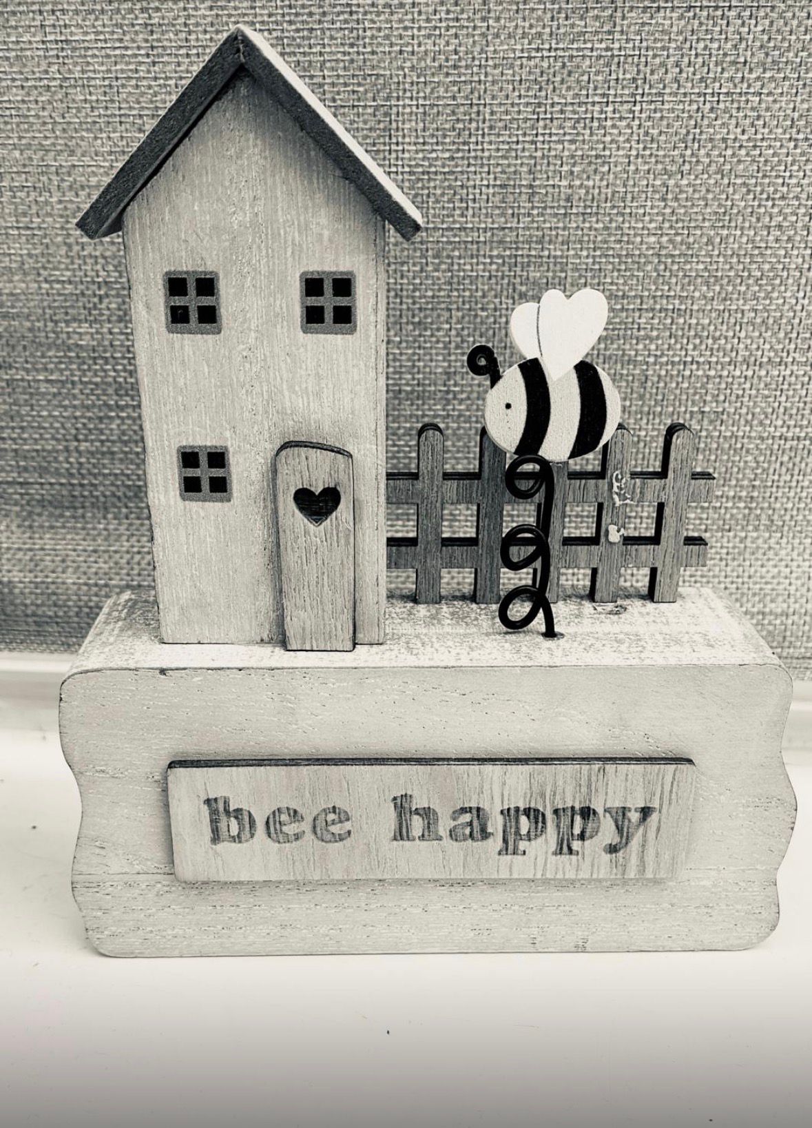 A small wooden house and a hand-painted bee on a sign reading 'bee happy'